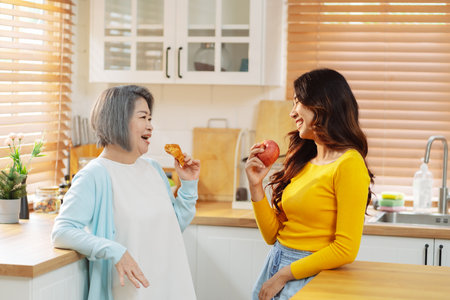 Happy asian woman daughter hugging senior mother in the kitchen room eating healthy food happy enjoying.の写真素材