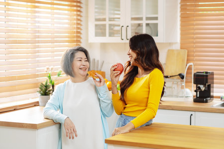 Happy asian woman daughter hugging senior mother in the kitchen room eating healthy food happy enjoying.の写真素材