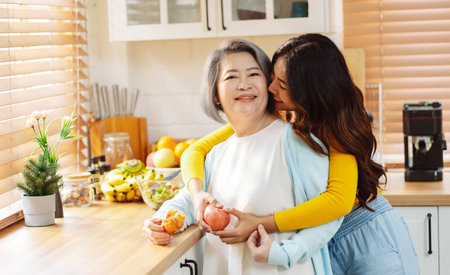 Happy asian woman daughter hugging senior mother in the kitchen room eating healthy food happy enjoying.の写真素材