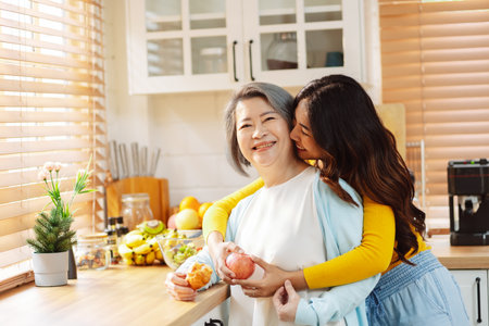Happy asian woman daughter hugging senior mother in the kitchen room eating healthy food happy enjoying.の写真素材