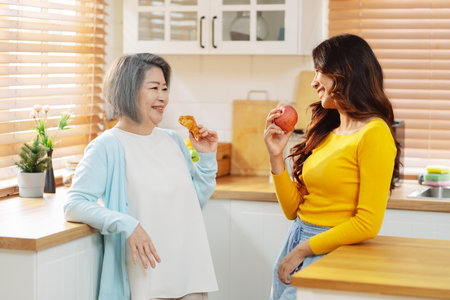 Happy asian woman daughter hugging senior mother in the kitchen room eating healthy food happy enjoying.の写真素材
