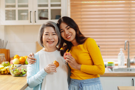 Happy asian woman daughter hugging senior mother in the kitchen room eating healthy food happy enjoying.の写真素材