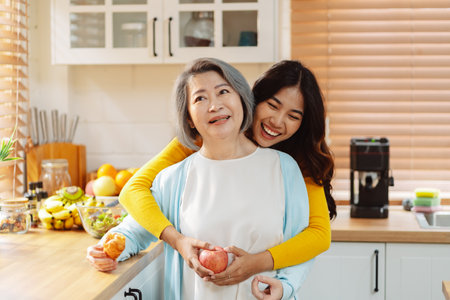 Happy asian woman daughter hugging senior mother in the kitchen room eating healthy food happy enjoying.の写真素材