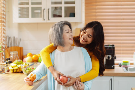 Happy asian woman daughter hugging senior mother in the kitchen room eating healthy food happy enjoying.の写真素材