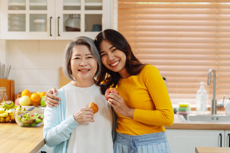 Happy asian woman daughter hugging senior mother in the kitchen room eating healthy food happy enjoying.の写真素材