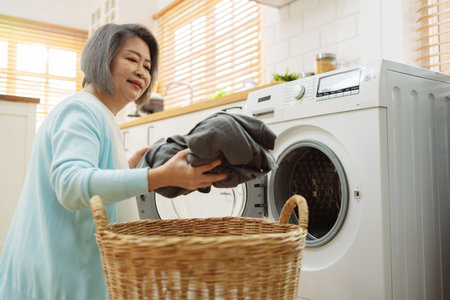 Asian Senior woman housekeeper loading clothes to washing machine. Routine activity in house concept.の写真素材