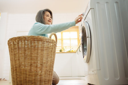 Asian Senior woman housekeeper loading clothes to washing machine. Routine activity in house concept.の写真素材