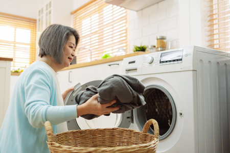 Asian Senior woman housekeeper loading clothes to washing machine. Routine activity in house concept.の写真素材