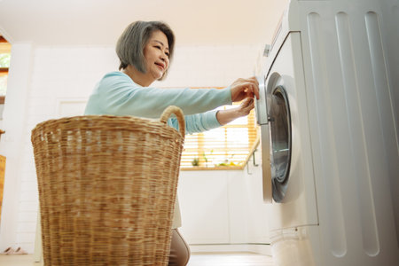 Asian Senior woman housekeeper loading clothes to washing machine. Routine activity in house concept.の写真素材
