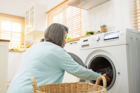 Asian Senior woman housekeeper loading clothes to washing machine. Routine activity in house concept.の写真素材