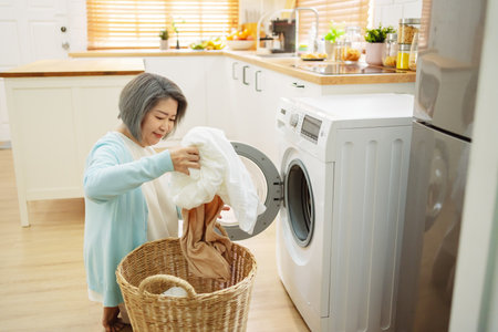 Asian Senior woman housekeeper loading clothes to washing machine. Routine activity in house concept.の写真素材