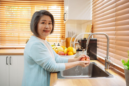 Happy asian senior mature woman washing fruits in the kitchen room before eating.の写真素材