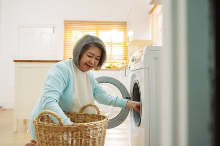 Asian Senior woman housekeeper loading clothes to washing machine. Routine activity in house concept.の写真素材
