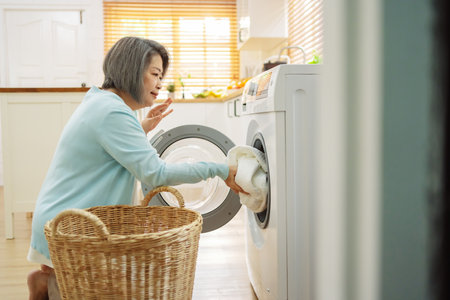 Asian Senior woman housekeeper loading clothes to washing machine. Routine activity in house concept.の写真素材