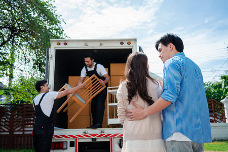 Asian Couple check while unloading boxes and furniture from a pickup truck to a new house with service cargo two men movers worker in uniform lifting boxes. concept of Home moving and delivery.の写真素材