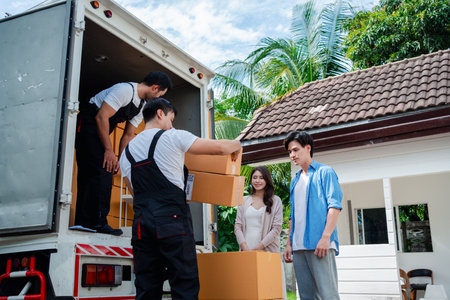 Asian Couple check while unloading boxes and furniture from a pickup truck to a new house with service cargo two men movers worker in uniform lifting boxes. concept of Home moving and delivery.の写真素材