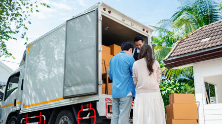 Asian Couple check while unloading boxes and furniture from a pickup truck to a new house with service cargo two men movers worker in uniform lifting boxes. concept of Home moving and delivery.の写真素材
