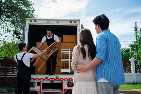 Asian Couple check while unloading boxes and furniture from a pickup truck to a new house with service cargo two men movers worker in uniform lifting boxes. concept of Home moving and delivery.の写真素材
