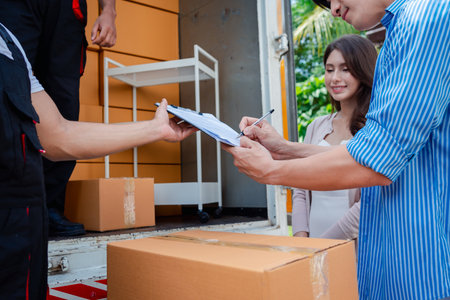 Asian Couple check while unloading boxes and furniture from a pickup truck to a new house with service cargo two men movers worker in uniform lifting boxes. concept of Home moving and delivery.の写真素材