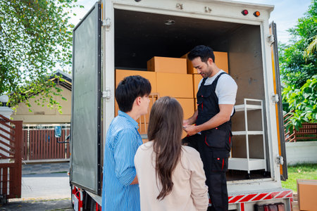 Asian Couple check while unloading boxes and furniture from a pickup truck to a new house with service cargo two men movers worker in uniform lifting boxes. concept of Home moving and delivery.の写真素材