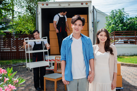 Asian Couple check while unloading boxes and furniture from a pickup truck to a new house with service cargo two men movers worker in uniform lifting boxes. concept of Home moving and delivery.の写真素材
