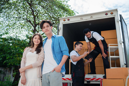 Asian Couple check while unloading boxes and furniture from a pickup truck to a new house with service cargo two men movers worker in uniform lifting boxes. concept of Home moving and delivery.の写真素材
