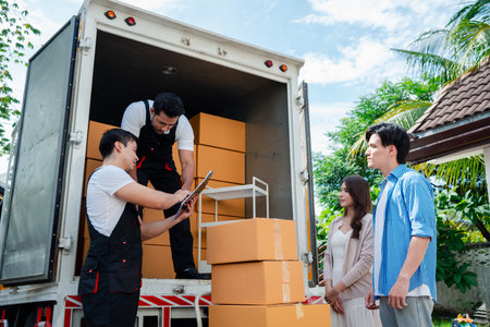 Asian Couple check while unloading boxes and furniture from a pickup truck to a new house with service cargo two men movers worker in uniform lifting boxes. concept of Home moving and delivery.の写真素材