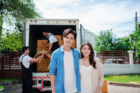 Asian Couple check while unloading boxes and furniture from a pickup truck to a new house with service cargo two men movers worker in uniform lifting boxes. concept of Home moving and delivery.の写真素材