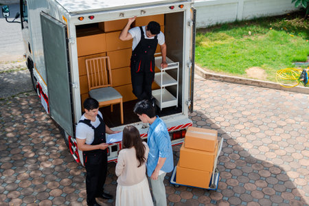 Asian Couple check while unloading boxes and furniture from a pickup truck to a new house with service cargo two men movers worker in uniform lifting boxes. concept of Home moving and delivery.の写真素材