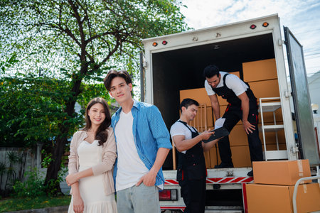 Asian Couple check while unloading boxes and furniture from a pickup truck to a new house with service cargo two men movers worker in uniform lifting boxes. concept of Home moving and delivery.の写真素材