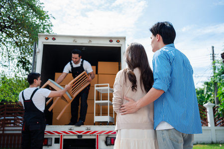 Asian Couple check while unloading boxes and furniture from a pickup truck to a new house with service cargo two men movers worker in uniform lifting boxes. concept of Home moving and delivery.の写真素材
