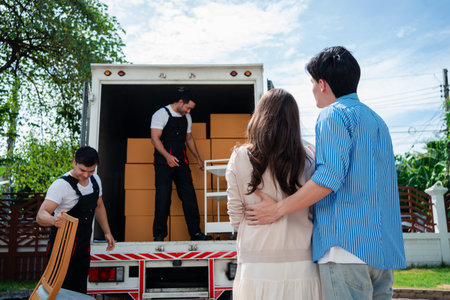 Asian Couple check while unloading boxes and furniture from a pickup truck to a new house with service cargo two men movers worker in uniform lifting boxes. concept of Home moving and delivery.の写真素材