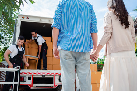Asian Couple check while unloading boxes and furniture from a pickup truck to a new house with service cargo two men movers worker in uniform lifting boxes. concept of Home moving and delivery.の写真素材