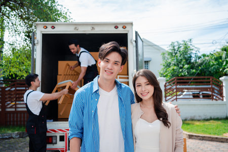Asian Couple check while unloading boxes and furniture from a pickup truck to a new house with service cargo two men movers worker in uniform lifting boxes. concept of Home moving and delivery.の写真素材