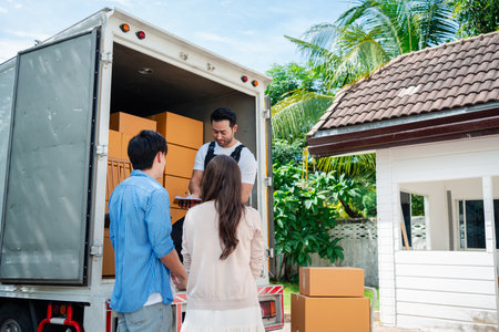 Asian Couple check while unloading boxes and furniture from a pickup truck to a new house with service cargo two men movers worker in uniform lifting boxes. concept of Home moving and delivery.の写真素材