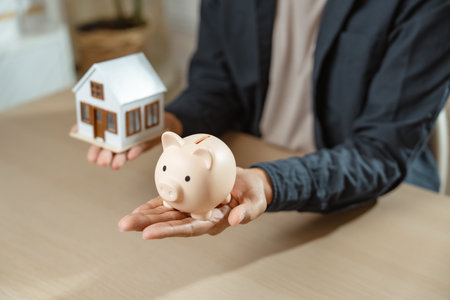 Investing in property or real estate financial concept. Man calculate planning strategy and income profit with house model for make money or create wealth.の写真素材