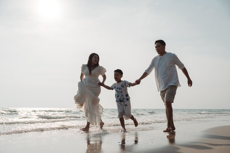 Happy asian family enjoy together on the beach in holiday vacation. family holding hands enjoying the sunset on the sea beach. Happy family travel, trip  family holidays weekend.の写真素材