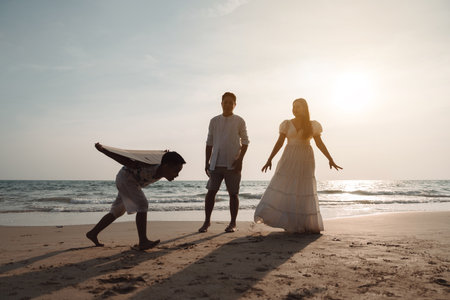 Happy asian family enjoy together on the beach in holiday vacation. Silhouette of the family holding hands enjoying the sunset on the sea beach. Happy family travel, trip family holidays weekend.の写真素材