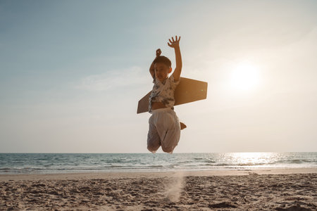 Happy boy with toy cardboard airplane play and jumping on the beach. Child enjoy on vacation creativity lifestyle of kid.の写真素材
