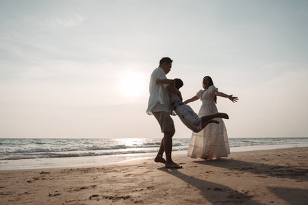 Happy asian family enjoy together on the beach in holiday vacation. Silhouette of the family holding hands enjoying the sunset on the sea beach. Happy family travel, trip  family holidays weekend.の写真素材