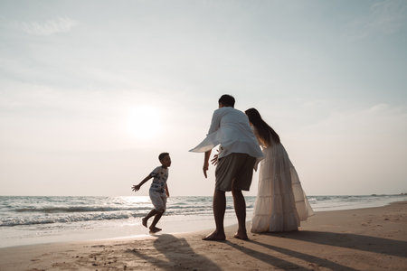 Happy asian family enjoy together on the beach in holiday vacation. Silhouette of the family holding hands enjoying the sunset on the sea beach. Happy family travel, trip  family holidays weekend.の写真素材