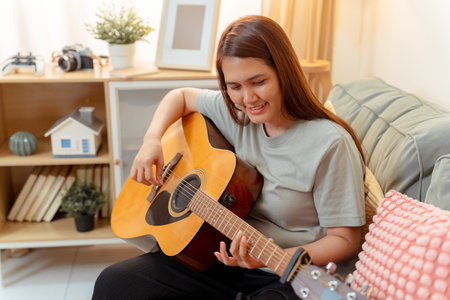 Woman Asian Playing Music Guitar Lifestyle Relax Lesson Fun Relaxation, Cheerful Moment of Home Guitar Practice, Sharing Joy and Music in a Cozy Living Room with Acousticの写真素材