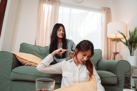 Asian Woman Home Massaging Shoulder Spa Treatment Wellness Togetherness Therapy, Serene Moment of Care and Connection as Two Friends Share Relaxation and Support in a Cozy Living Room Settingの写真素材