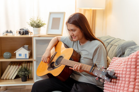 Woman Asian Playing Music Guitar Lifestyle Relax Lesson Fun Relaxation, Cheerful Moment of Home Guitar Practice, Sharing Joy and Music in a Cozy Living Room with Acousticの写真素材