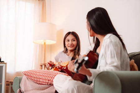 Asian Woman Music Guitar Playing Togetherness Song Teenage Indoor Living Room, Joyful Gathering of Friends Sharing Music, Laughter, and Relaxation Through Guitar Playing at Homeの写真素材