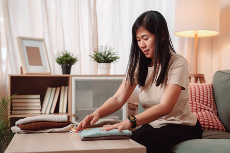 Woman Folded Stack Clothes Housework Female Laundry Lifestyle Housewife, Folding Freshly Washed Clothes into a Neat Stack, Embracing a Comfortable Domestic Life with a Smile at Homeの写真素材