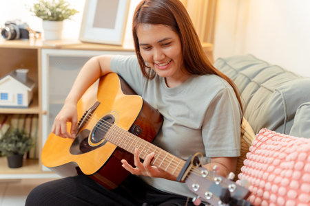 Woman Asian Playing Music Guitar Lifestyle Relax Lesson Fun Relaxation, Cheerful Moment of Home Guitar Practice, Sharing Joy and Music in a Cozy Living Room with Acousticの写真素材