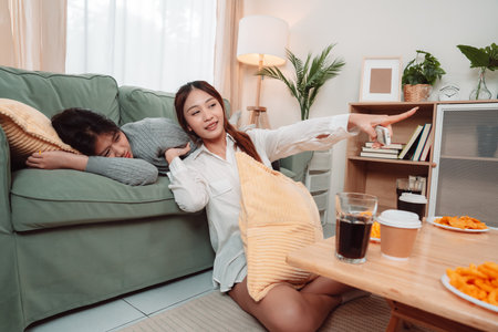 Asian Women Snack Food Eating Lifestyle Indoor Living Room Enjoyment Movie, Two Young Adults Sharing Laughter and Snacks While Watching TV, Embracing Friendship and Relaxation at Home Togetherの写真素材