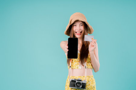 Asian Woman Ticket Credit Online Trip Journey Joy Camera Positive Rest, A Cheerful Young Traveler Posing with Ticket and Credit Card, Ready for a Stylish Summer Adventure on blue studio backgroundの写真素材