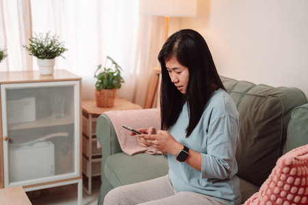 Woman Asian Playing Social Media Internet Smartphone Phone People Indoor Mobile Phone, Young Female Enjoys Online Moments, Smiling and Relaxing on the Sofa While Connectingの写真素材